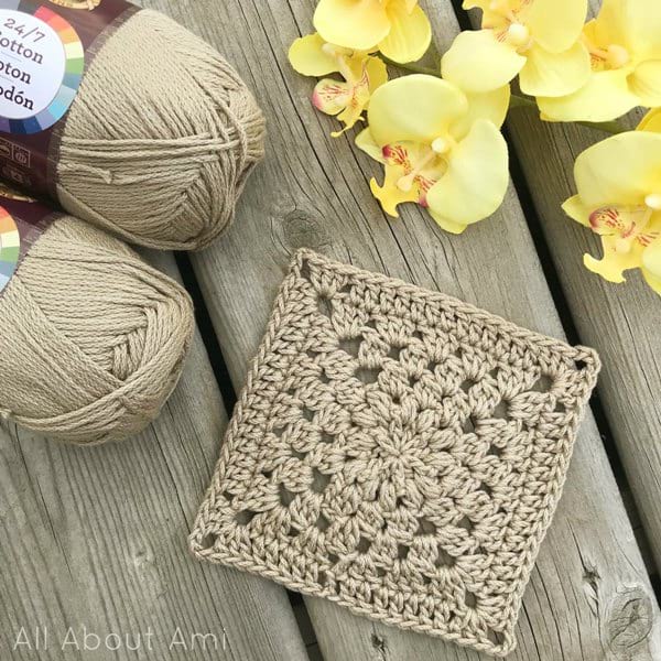 a crochet square next to yarns and flowers